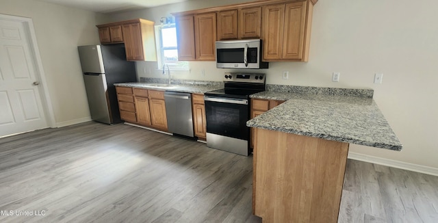 2708 Canty St, Pascagoula, MS 39567 - kitchen featuring appliances with stainless steel finishes, a peninsula, light wood finished floors, brown cabinets, and light stone countertops