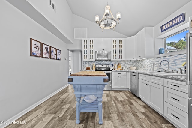 kitchen with appliances with stainless steel finishes, hanging light fixtures, white cabinetry, hardwood / wood-style floors, and wooden counters