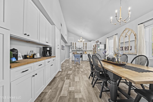 dining room with light hardwood / wood-style floors, lofted ceiling, and an inviting chandelier