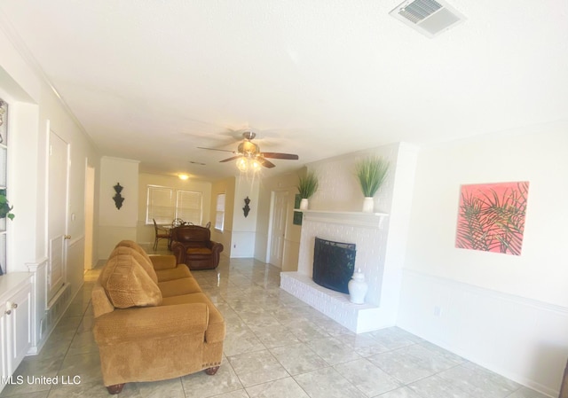 living area featuring light tile patterned floors, a brick fireplace, visible vents, and a ceiling fan