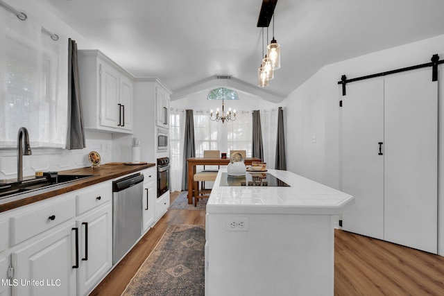 kitchen with a barn door, vaulted ceiling, black appliances, pendant lighting, and light hardwood / wood-style floors