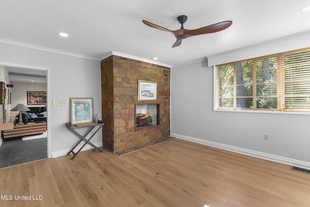 unfurnished living room featuring ceiling fan, a stone fireplace, wood-type flooring, and ornamental molding