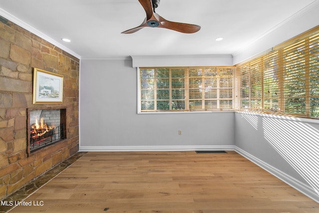 unfurnished room with a stone fireplace, crown molding, hardwood / wood-style flooring, and ceiling fan