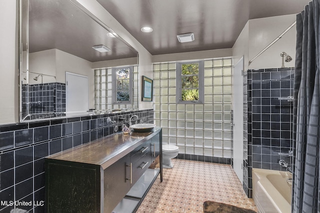 full bathroom with tile walls, vanity, tiled shower / bath, and toilet