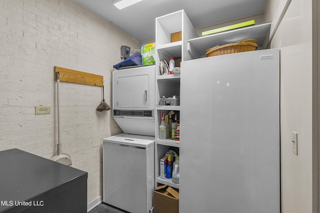 laundry area featuring brick wall and stacked washing maching and dryer