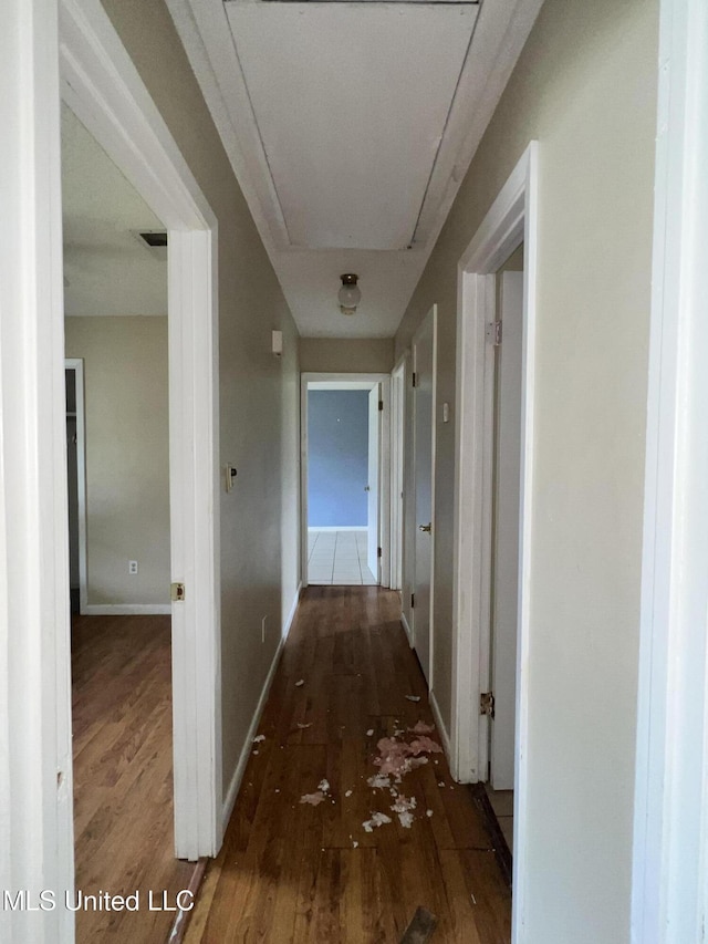 corridor with baseboards, attic access, and wood finished floors