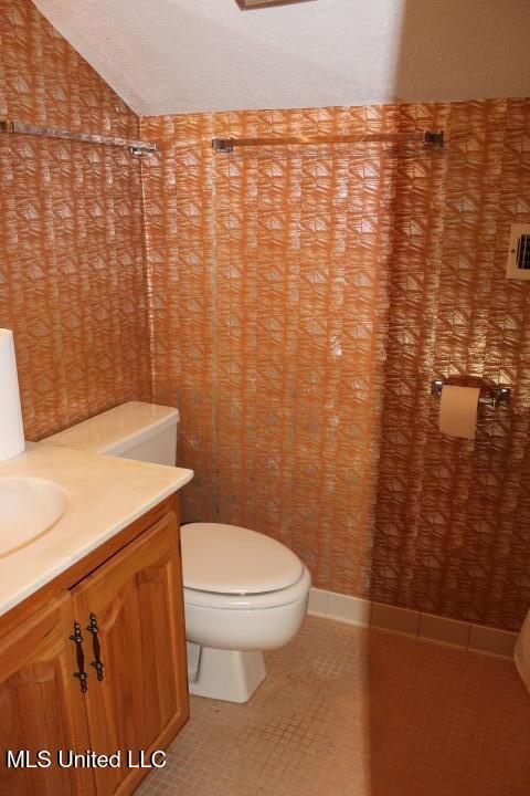 bathroom with tile patterned floors, lofted ceiling, toilet, and vanity