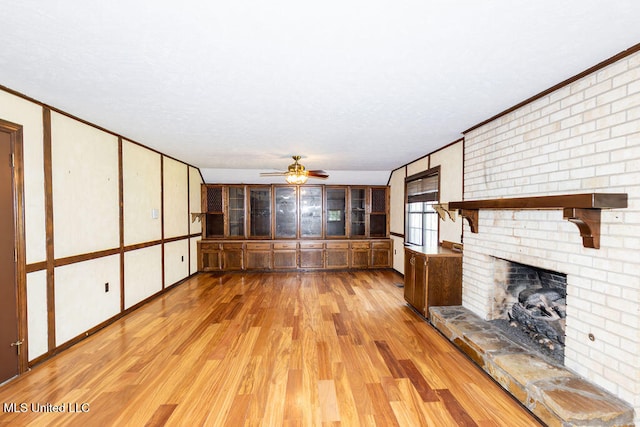 unfurnished living room with light hardwood / wood-style floors, crown molding, a fireplace, and ceiling fan