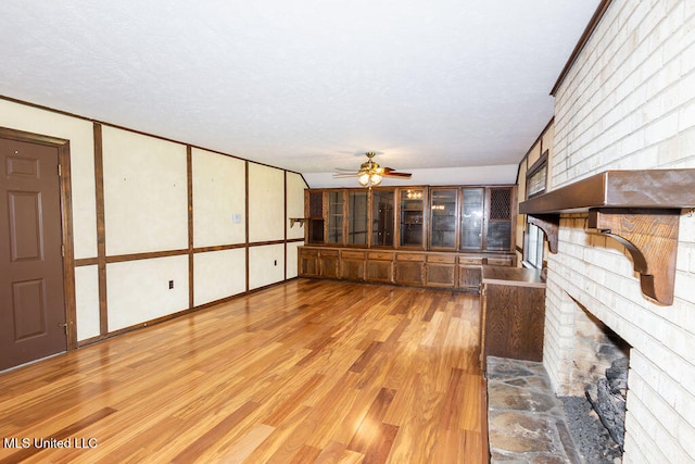 unfurnished living room featuring light hardwood / wood-style flooring, a brick fireplace, a textured ceiling, and ceiling fan