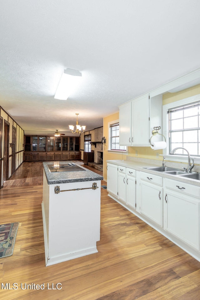 kitchen with white cabinets, a textured ceiling, sink, light hardwood / wood-style floors, and a center island