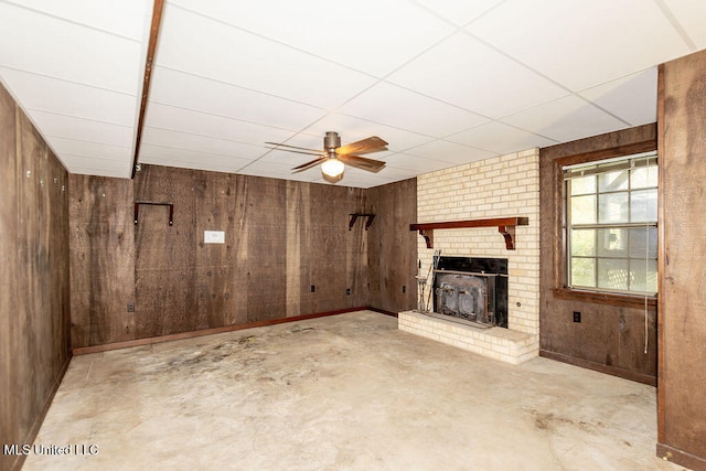 unfurnished living room featuring ceiling fan, wood walls, and a brick fireplace