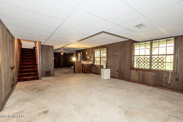 basement featuring a drop ceiling, wood walls, and ceiling fan