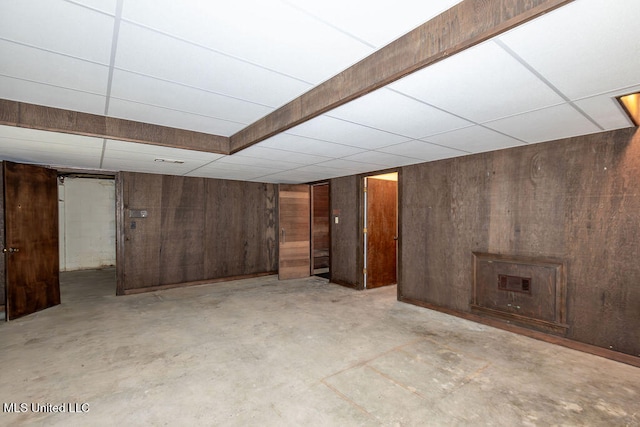 basement featuring wooden walls and a paneled ceiling