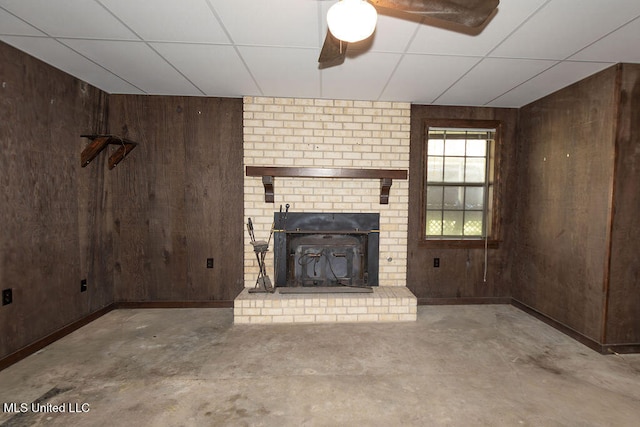 unfurnished living room with a paneled ceiling, wooden walls, and a fireplace