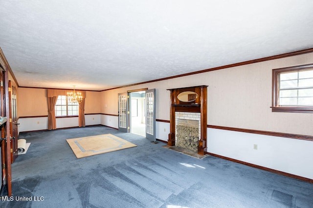 empty room with a fireplace, a textured ceiling, dark colored carpet, crown molding, and a chandelier