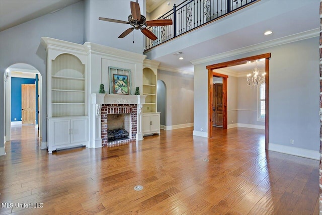 living area featuring arched walkways, ceiling fan with notable chandelier, a brick fireplace, and wood finished floors