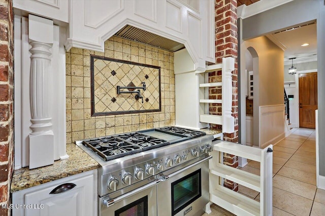 kitchen featuring light tile patterned floors, light stone countertops, range with two ovens, white cabinets, and tasteful backsplash