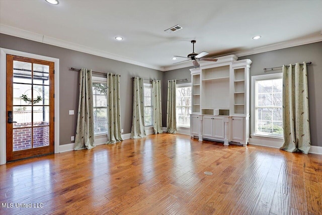 unfurnished living room with a wealth of natural light, visible vents, ornamental molding, light wood-style flooring, and ceiling fan