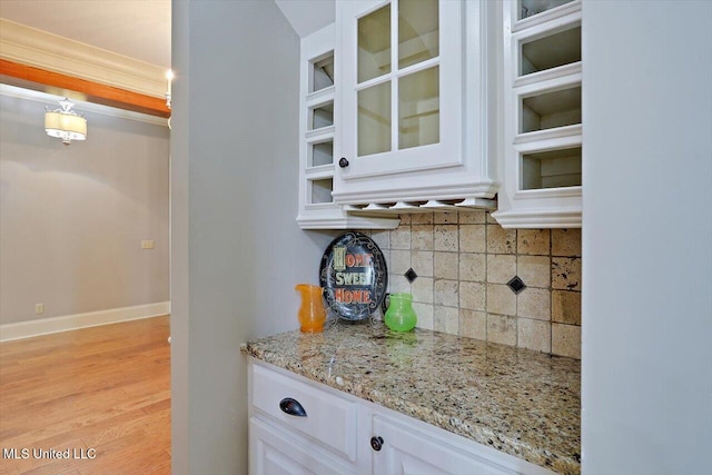 kitchen with tasteful backsplash, white cabinets, glass insert cabinets, and light stone counters