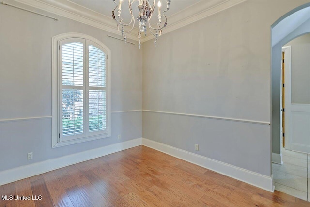 unfurnished room featuring light wood finished floors, baseboards, ornamental molding, an inviting chandelier, and arched walkways