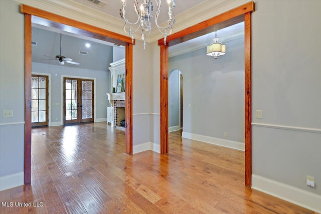 empty room featuring visible vents, ceiling fan with notable chandelier, wood finished floors, arched walkways, and a fireplace