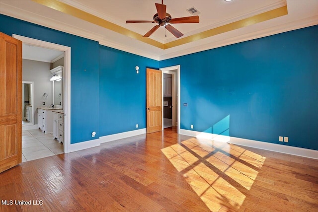 unfurnished room featuring a ceiling fan, a raised ceiling, wood finished floors, and ornamental molding