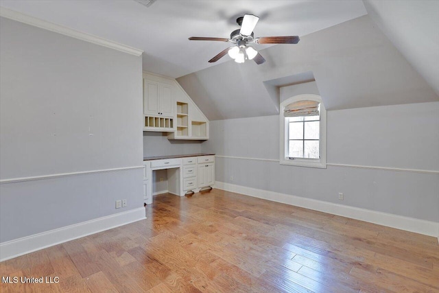 unfurnished office featuring light wood-style floors, ceiling fan, built in desk, and vaulted ceiling