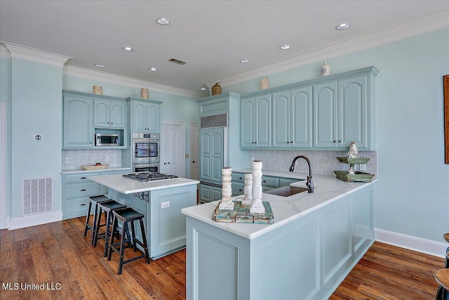 kitchen featuring a sink, appliances with stainless steel finishes, visible vents, a kitchen bar, and backsplash