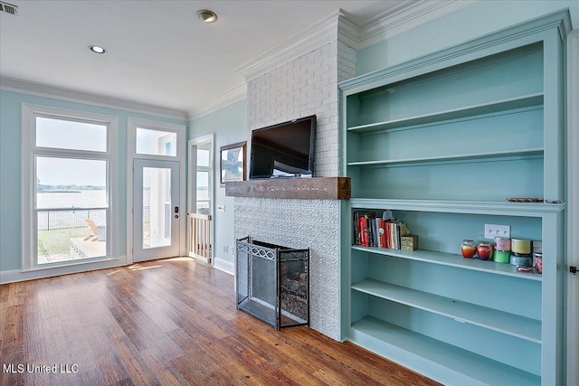 unfurnished living room with ornamental molding, built in shelves, a brick fireplace, and hardwood / wood-style flooring