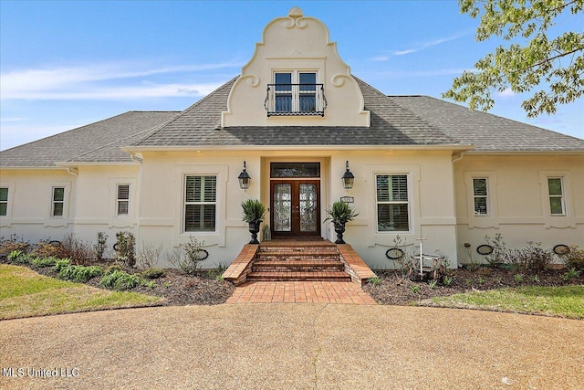 view of front of home with french doors, stucco siding, and roof with shingles