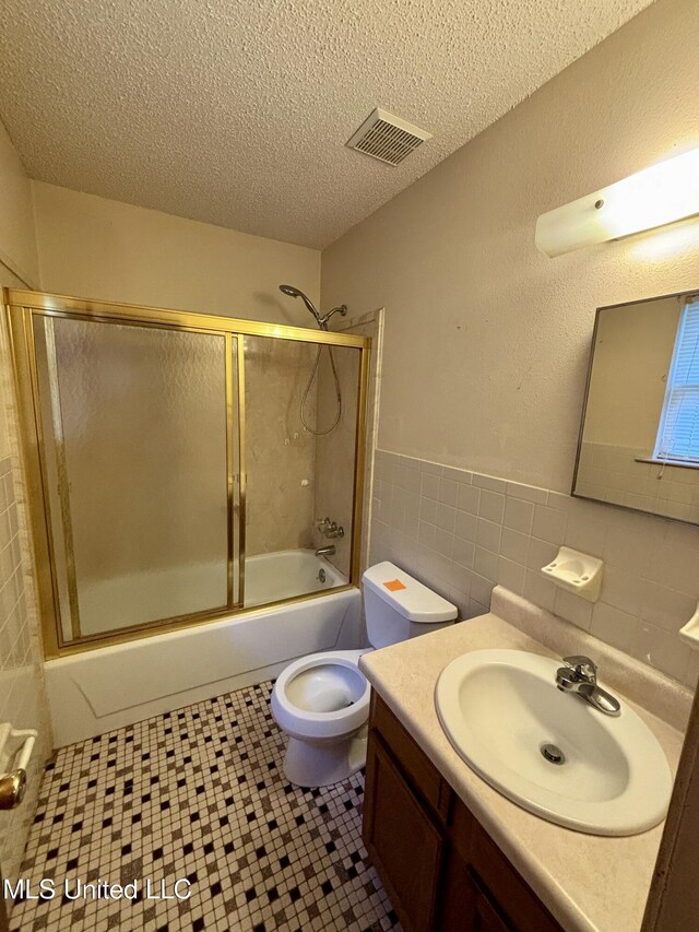 126 Faust Dr, Gulfport, MS 39503 - bathroom featuring tile walls, vanity, combined bath / shower with glass door, toilet, and a textured ceiling