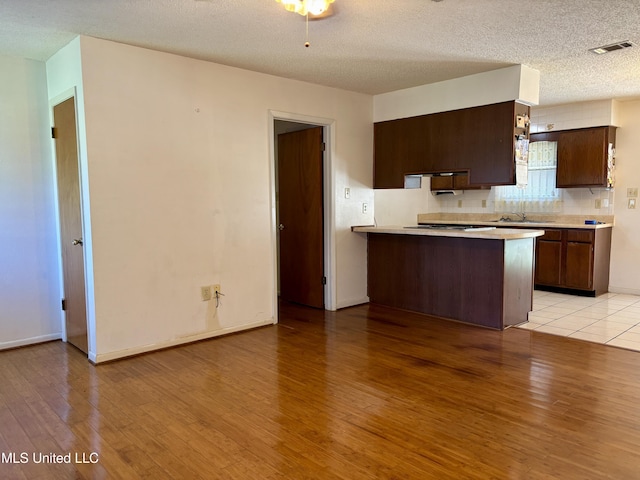 126 Faust Dr, Gulfport, MS 39503 - kitchen with light countertops, light wood-style flooring, dark brown cabinets, a peninsula, and a textured ceiling