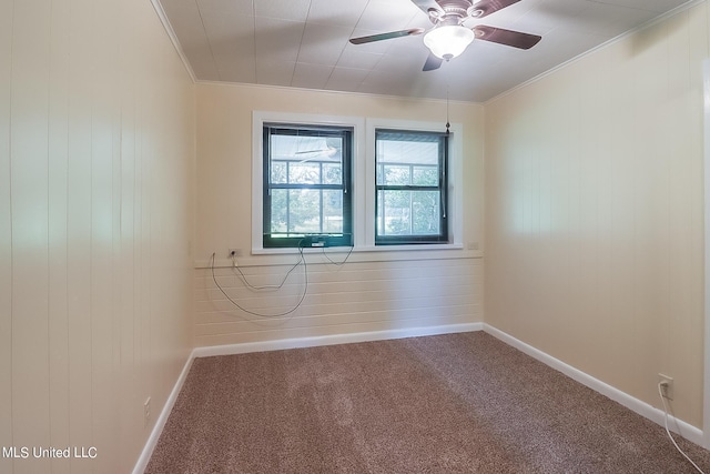 carpeted empty room featuring wood walls, ornamental molding, and ceiling fan