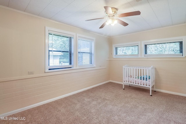 unfurnished bedroom featuring ornamental molding, a nursery area, carpet flooring, and ceiling fan