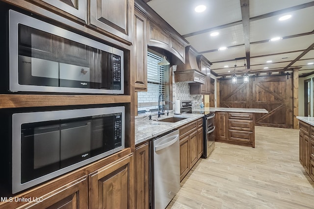 kitchen with appliances with stainless steel finishes, sink, light wood-type flooring, a barn door, and backsplash