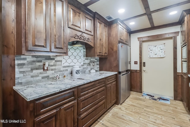 kitchen with decorative backsplash, beam ceiling, light hardwood / wood-style flooring, stainless steel fridge, and light stone countertops