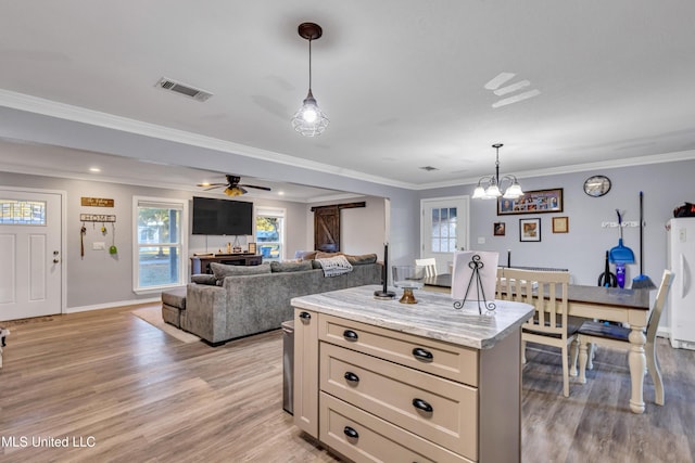 kitchen featuring ornamental molding, a barn door, hanging light fixtures, and light stone countertops