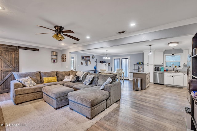 living room featuring ceiling fan with notable chandelier, sink, light wood-type flooring, crown molding, and a barn door