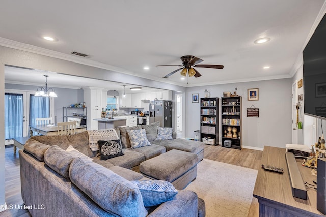 living room featuring crown molding, ceiling fan with notable chandelier, light hardwood / wood-style flooring, and sink