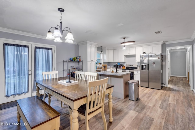 dining space featuring light wood-type flooring, crown molding, french doors, and a notable chandelier