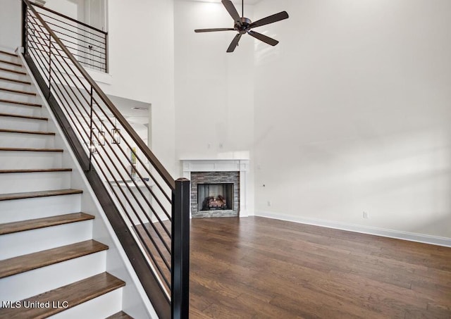 staircase featuring ceiling fan, a stone fireplace, wood-type flooring, and a high ceiling