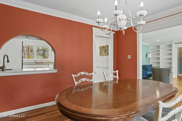 dining space featuring built in shelves, wood finished floors, baseboards, an inviting chandelier, and crown molding