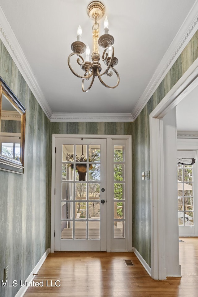 entryway with wallpapered walls, visible vents, wood finished floors, crown molding, and a chandelier