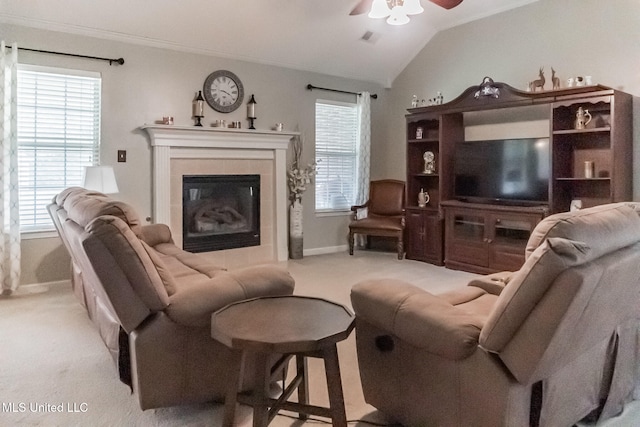 living room with ceiling fan, a tiled fireplace, vaulted ceiling, and light colored carpet