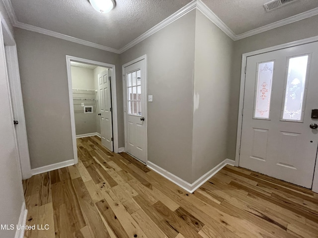 entrance foyer featuring a textured ceiling, visible vents, ornamental molding, and light wood-type flooring
