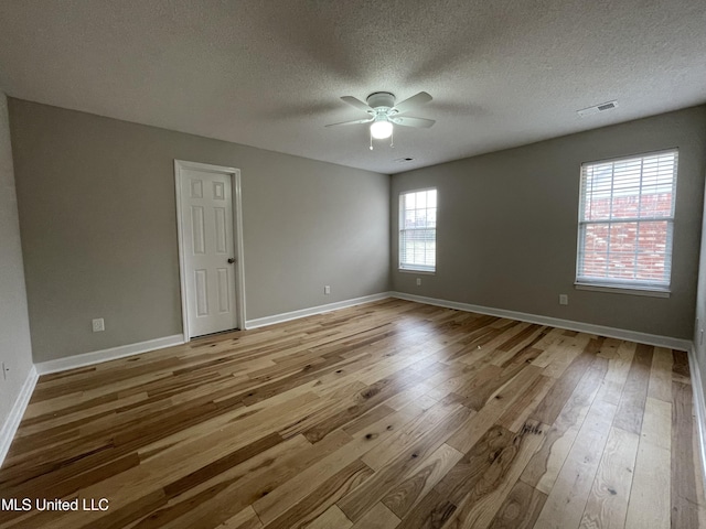 spare room featuring visible vents, a ceiling fan, wood-type flooring, and a textured ceiling