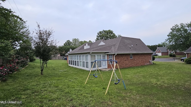 back of property featuring brick siding, a shingled roof, a playground, and a yard