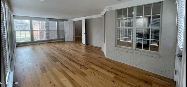 unfurnished room with baseboards, brick wall, and wood finished floors