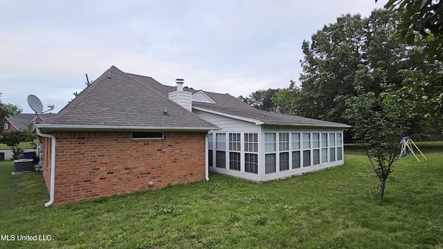 rear view of house with a shingled roof, a chimney, a yard, and brick siding