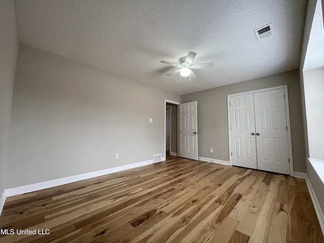 unfurnished bedroom with a textured ceiling, visible vents, wood finished floors, baseboards, and a closet